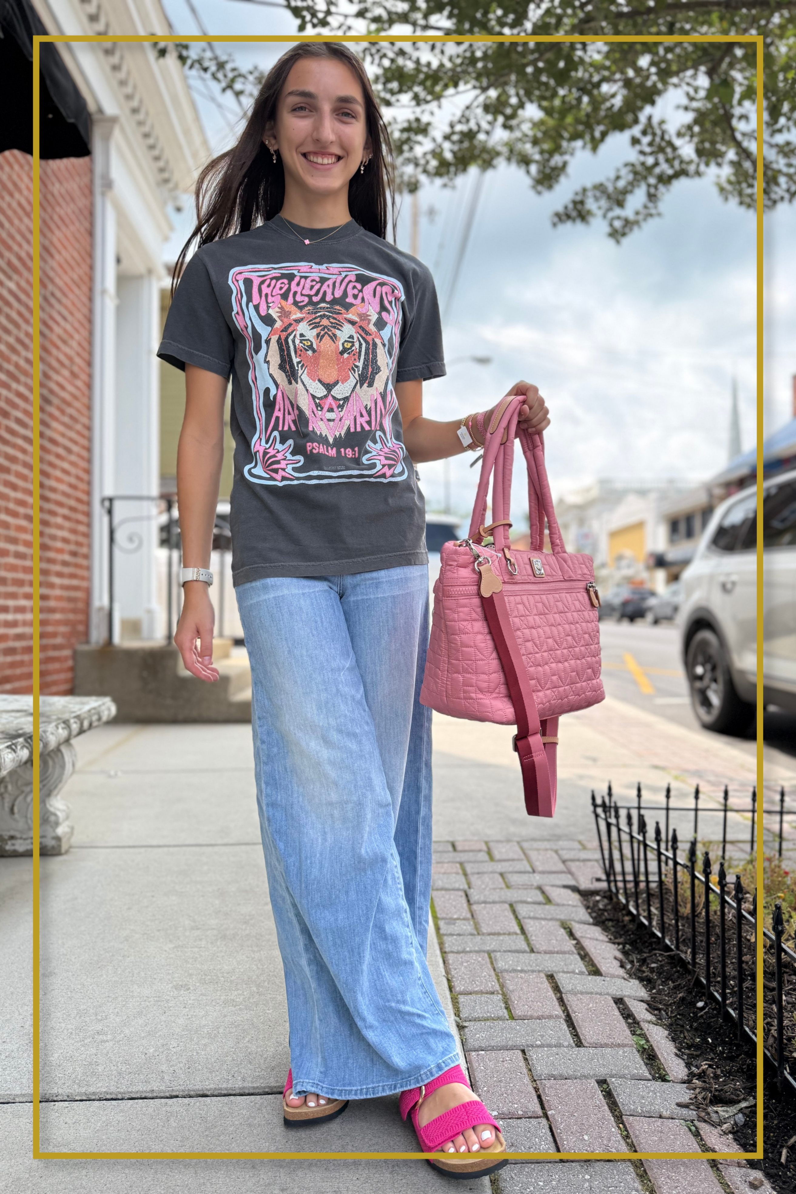 Woman in a fireworks-print zip dress with pink flamingo crossbody bag and cat-eye sunglasses outside a storefront
