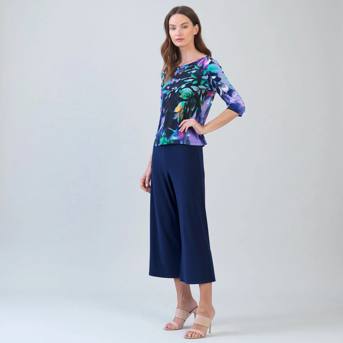 Woman wearing a colorful floral top and navy pants on a light gray background